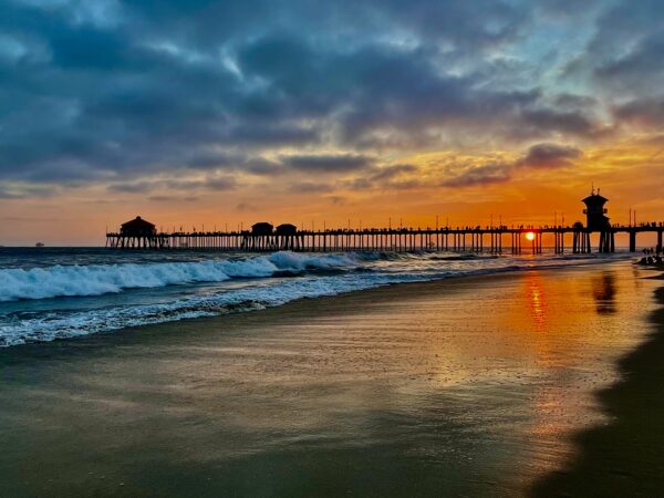 A pier is shown at sunset on the beach.