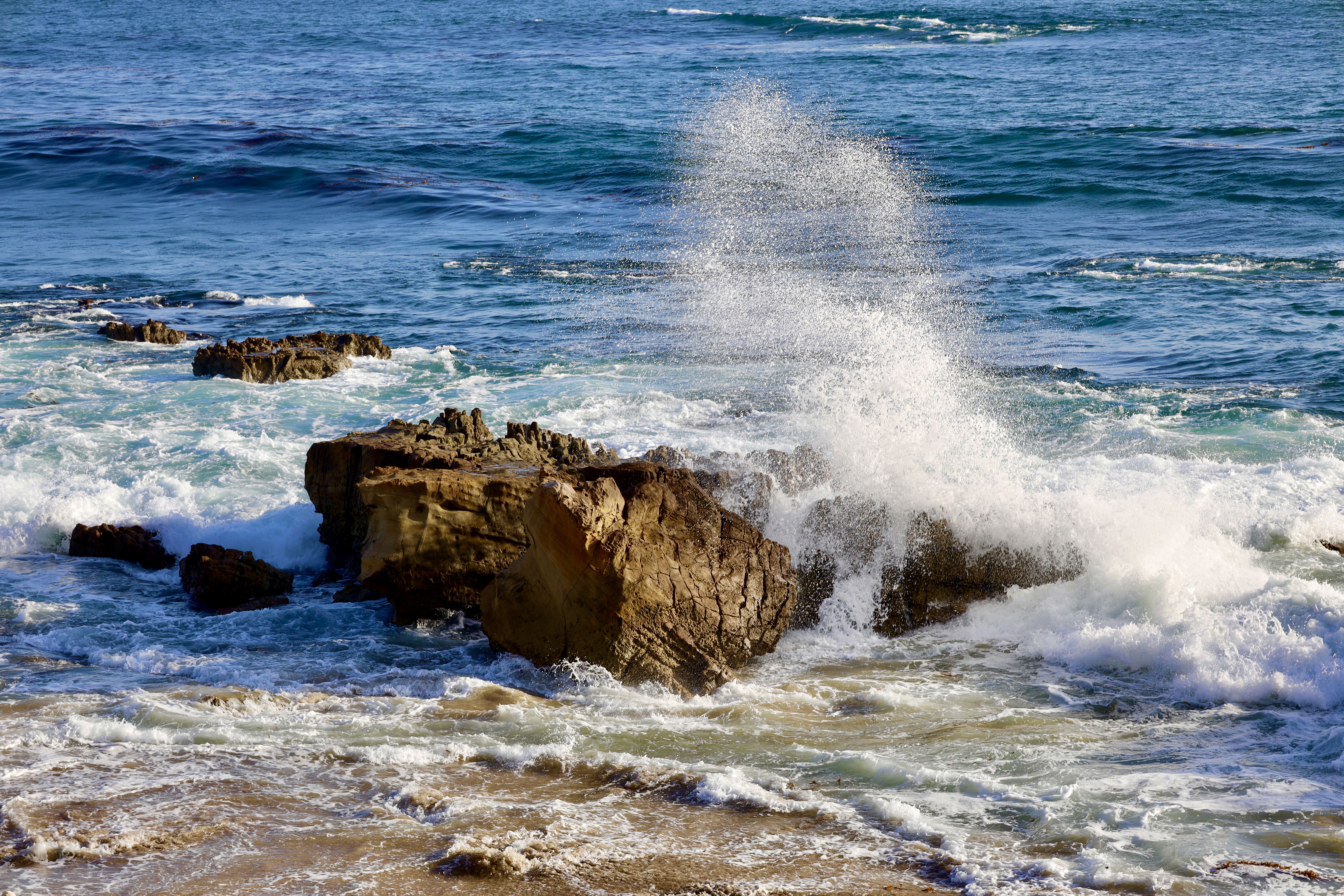 A large rock in the ocean with waves crashing on it.