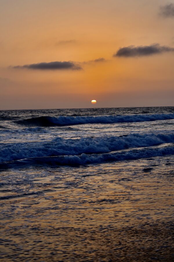 A sunset over the ocean with waves crashing on it.